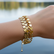 Gold bracelets on a wrist with a blurred natural background